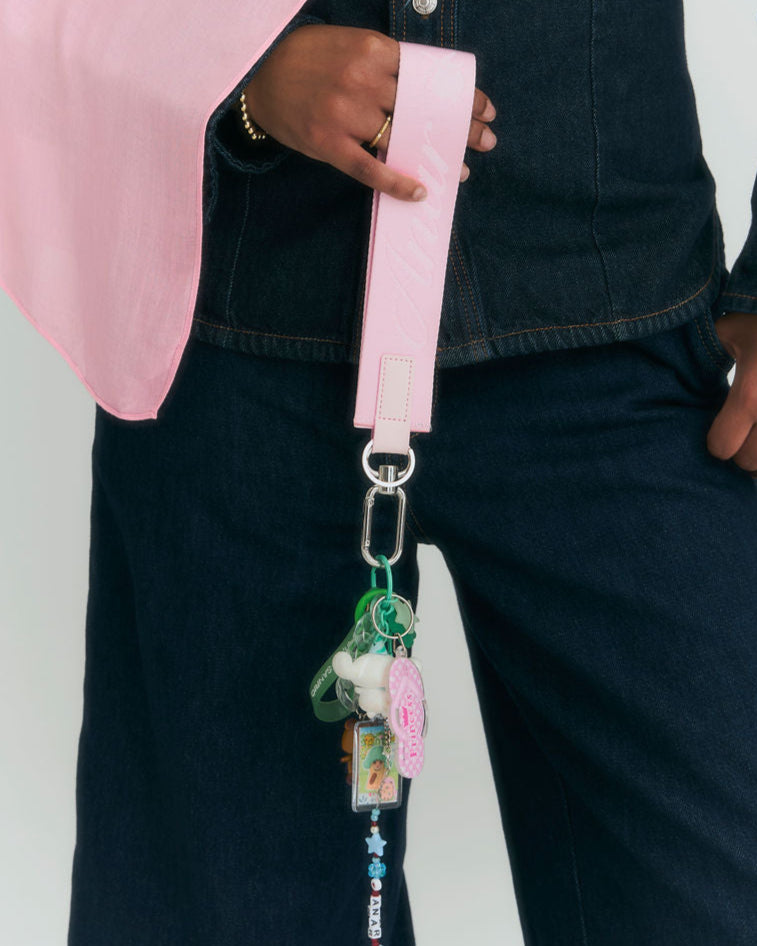 Person holding a pink strap with decorative charms against a neutral background